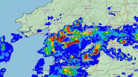 Met Office Weather map showing areas of blue and higher intensity areas with red where the heavier rain will be. these areas are Barnstaple, Minehead, Cardiff, Swansea, Merthyr Tydfil. 