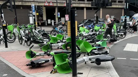 Tom Bower Around a dozen dockless e-bikes lie on their sides on a traffic island in Tower Hill where several more have been crammed into a small area of pavement that is blocking pedestrians from crossing