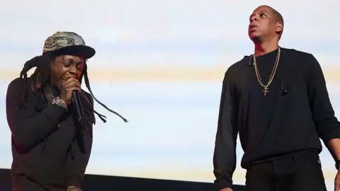 Getty Images Lil Wayne and Jay-Z, both dressed in black, performing together on stage