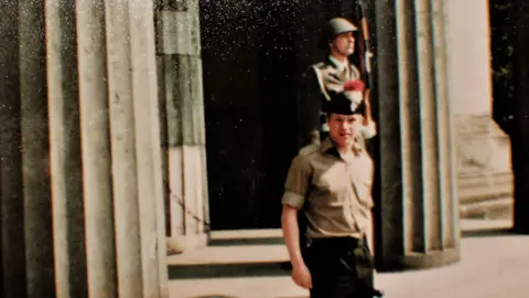 Stephen Close An archive picture of a soldier posing at the camera. In the background you can see a guardsman holding a rifle looking away from the camera