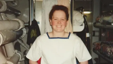 Emma Riley Picture taken in the early 90s of a young red-head in her Navy uniform. She is stood next to her bunk and smiling at the camera.