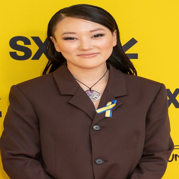 Karen Fukuhara wearing a dark suit with a blue and yellow ribbon on the red carpet at SXSW