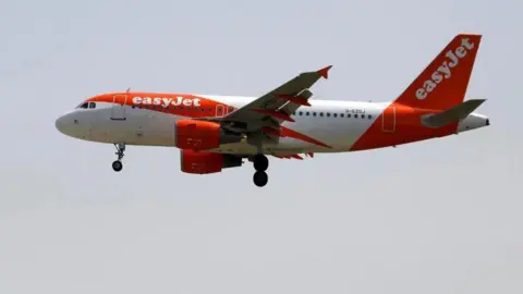 Reuters An easyJet-branded plane, with orange and white livery, is seen in flight against a light grey sky