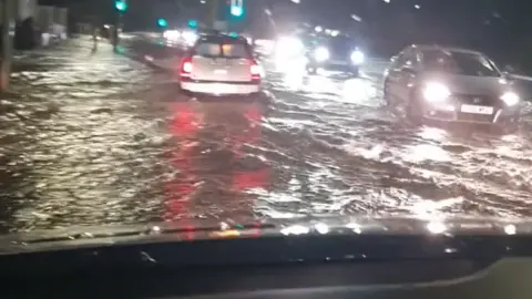 Joanne Butler A flooded road, with cars driving through water at night