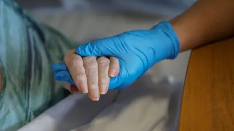 Getty Images A gloved hand holding an elderly person's hand