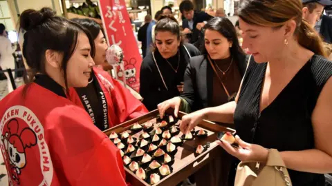 AFP A group of women pick peaches from a tray being held by two women in Japanese kimonos