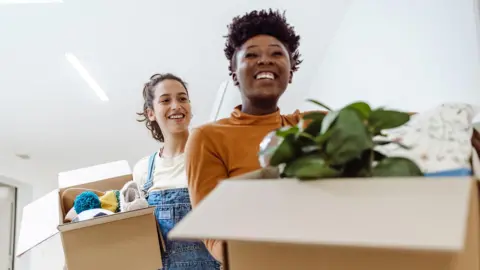 Getty Images Two students smile as they hold boxes of belongings